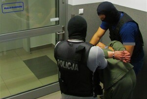 zdjęcie ilustracyjne- dwóch policjantów prowadzi osobę zatrzymaną