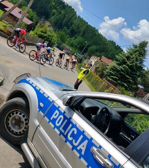 radiowóz, obok policjant kierujący ruchem oraz przejeżdżający kolarze