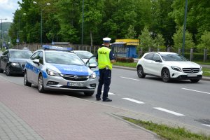 policjant ruchu drogowego, obok radiowóz i przejeżdżające samochody