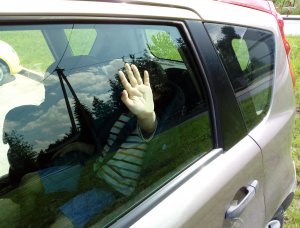 słoneczna pogoda, dziecko wewnątrz samochodu trzyma dłoń przy szybie