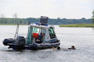policyjna łódź, policjant wyciąga dłoń do dwóch osób pływających w pobliżu