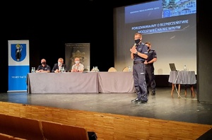 debata - przy stoliku siedzą policjant i samorządowcy, obok stoi dwóch funkcjonariuszy