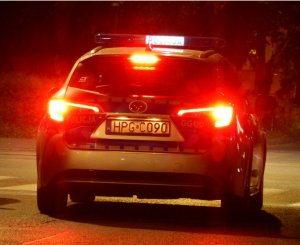 Radiowóz w porze nocnej – widok z tyłu samochodu. Widać podświetlony napis policja na dachu oraz na klapie tylnej nr rejestracyjny „HPGC090”. Samochód jest w ruchu, świecą się światła hamowania.