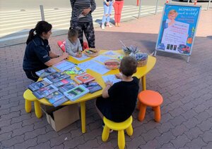przy stoliczku siedzi dwójka dzieci, obok policjantka