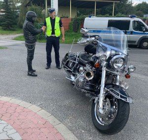 policjant wręcza motocykliście kartę, w tle zaparkowany radiowóz