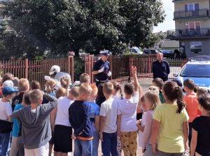 policyjny radiowóz, dwójka policjantów i uczniowie na szkolnym podwórku