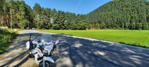 policyjny motocykl, w tle las i biegnący po jezdni zawodnicy