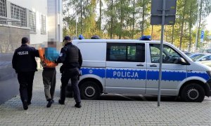 umundurowani policjanci prowadzą zatrzymanego do radiowozu