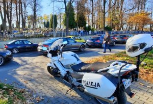 policyjny motocykl, na dalszym planie ruchliwa ulica, za nią cmentarz