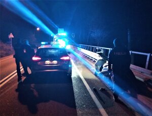 noc, błyskają lampy radiowozów, policjant prowadzi mężczyznę do pojazdu, obok stoi drugi funkcjonariusz