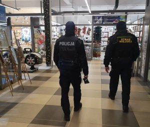 policjant i strażnik miejski kontrolują galerię handlową