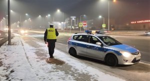 policjant ruchu drogowego z lampą do zatrzymywania pojazdów w nocy, obok oznakowany radiowóz