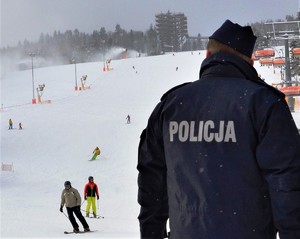 na pierwszym planie policjant prewencji odwrócony tyłem, w tle narciarze zjeżdżający ze stoku