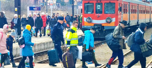 podróżni wysiedli z pociągu, umundurowany policjant niesie walizki