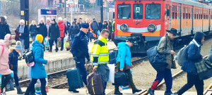 podróżni wysiedli z pociągu, umundurowany policjant niesie walizki