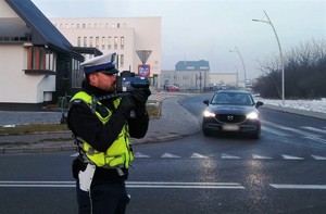policjant ruchu drogowego z laserowym miernikiem prędkości, w tle jadący samochód