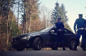 nieoznakowany radiowóz, obok policjanci odwróceni tyłem