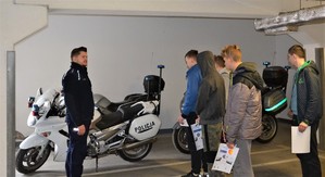 uczniowie oglądają policyjny motocykl zaparkowany w garażu podziemnym komendy, obok policjant Wydziału Prewencji