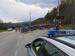 uczestnicy wyścigu przejeżdżający  przez przejazd kolejowy  obok  radiowóz Policji.