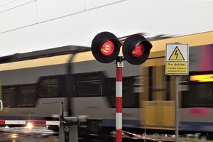sygnalizator drogowy przejazdu kolejowego nadający światło czerwone, w tle przejeżdżający pociąg - zdjęcie ilustracyjne
