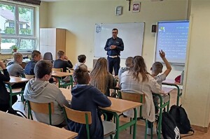 policjant podczas prelekcji, jeden z uczniów podnosząc rękę zgłasza się do odpowiedzi