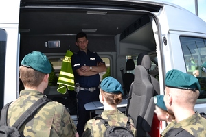policjant będący we wnętrzu radiowozu odpowiada na pytania młodzieży z klasy mundurowej
