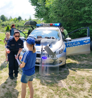 policjantka wręcza dziewczynce element odblaskowy, za nimi radiowóz