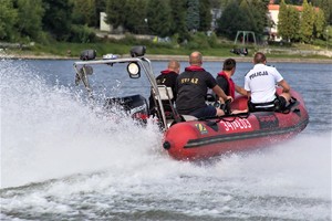 łódź strażacka płynąca po jeziorze, a w niej policjant i strażacy