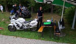 3. Umundurowany policjant na stoisku policyjnym, obok oznakowany motocykl, w tle quad