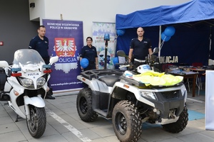 umundurowani policjanci na stoisku profilaktycznym, przed mini stoi motocykl oraz Quad