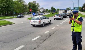 Umundurowany policjant z laserowym miernikiem prędkości, w tle jadące samochody