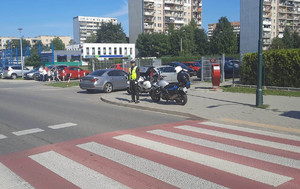 4.oznakowane przejście dla pieszych przy którym stoi umundurowany policjant  obok motocykl słuzbowy, w tle samochody i budynki