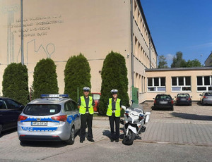 5. umundurowani policjanci podczas prowadzonych działań przy szkole podstawowej. obok oznakowany radiowóz