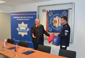 przedstawiciel IPA Albania wręcza upominek zastępcy komendanta, który w ręku trzyma granatową torebkę z logo sądeckiej Policji