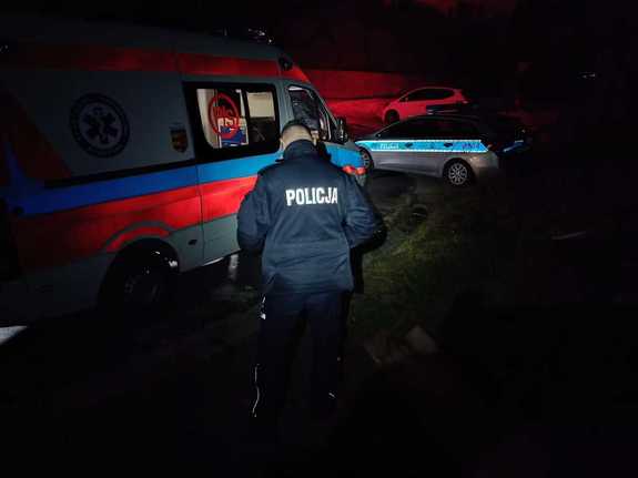 noc, policjant stoi obok karetki, dalej zaparkowany policyjny radiowóz