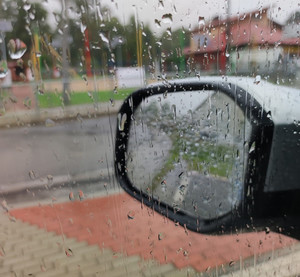 zdjęcie wykonane z wnętrza samochodu, lusterko i szyba mokre od deszczu