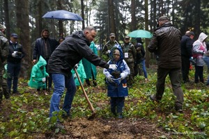 las, deszczowa aura, prezydent odbiera sadzonkę cisa z rąk małego chłopca, w tle uczestnicy akcji - fot. Kancelaria Prezydenta RP facebook