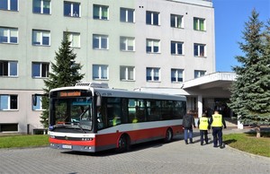 3. przed budynkiem oddziału stoi zaparkowany autobus miejski, obok policjanci w kamizelkach odblaskowych