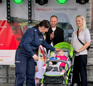 policjantka głaszcze po głowie małą dziewczynkę leżącą w wózku spacerowym, obok stoją rodzice dziewczynki