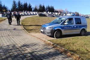 umundurowani policjanci patrolują rejon cmentarza, obok zaparkowany radiowóz