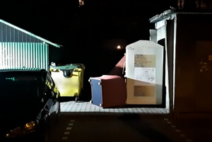 kontener z używaną odzieżą obok fotele i żółte pojemniki na śmieci przy wiacie