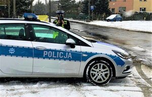 umundurowana policjantka ruchu drogowego z ręcznym miernikiem prędkości, obok oznakowany radiowóz