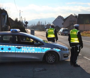 policjanci ruchu drogowego przy radiowozie, w tle jadący samochód