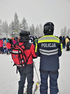 policyjny narciarz i goprowiec, w tle osoby czekające na wjazd na stok