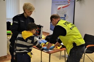 chłopiec odbija linie papilarne na pamiątkowym dyplomie, obok technik kryminalistyki i policjantka prewencji