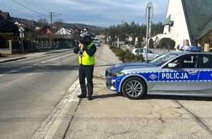 policjant ruchu drogowego z laserowym miernikiem prędkości, obok oznakowany radiowóz