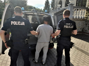 policjanci prowadzą zatrzymanego do radiowozu przed budynkiem Komisariatu Policji w Piwnicznej-Zdroju
