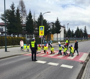 przedszkolaki w kamizelkach odblaskowych przechodzą przez przejście dla pieszych, obok policjanci