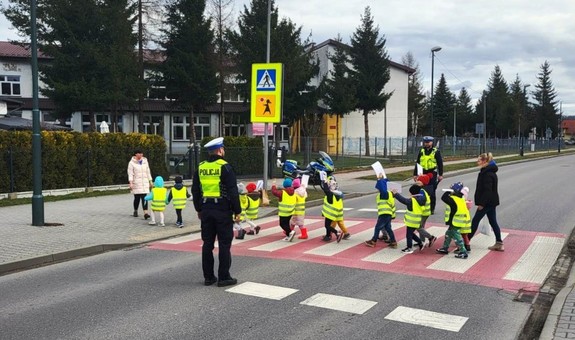 przedszkolaki w kamizelkach odblaskowych przechodzą przez przejśćie dla pieszych, obok policjanci — kopia