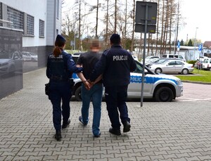 umundurowani policjantka oraz policjant prowadzą zatrzymanego w stronę oznakowanego radiowozu